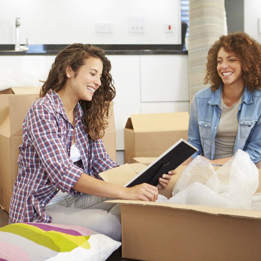 Two women unpacking a box in a bright kitchen
